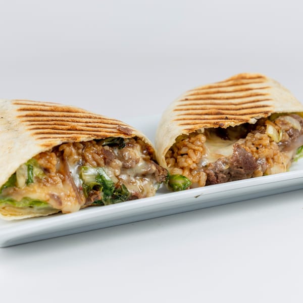 Two halves of a grilled burrito, revealing a filling of meat, rice, cheese, and greens.