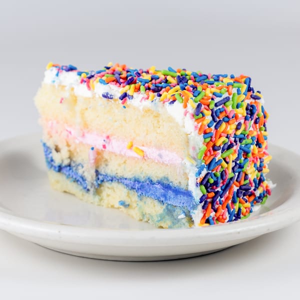 Slice of Kudo Society Cafe's vanilla cake with colorful sprinkles, pink and blue frosting layers.