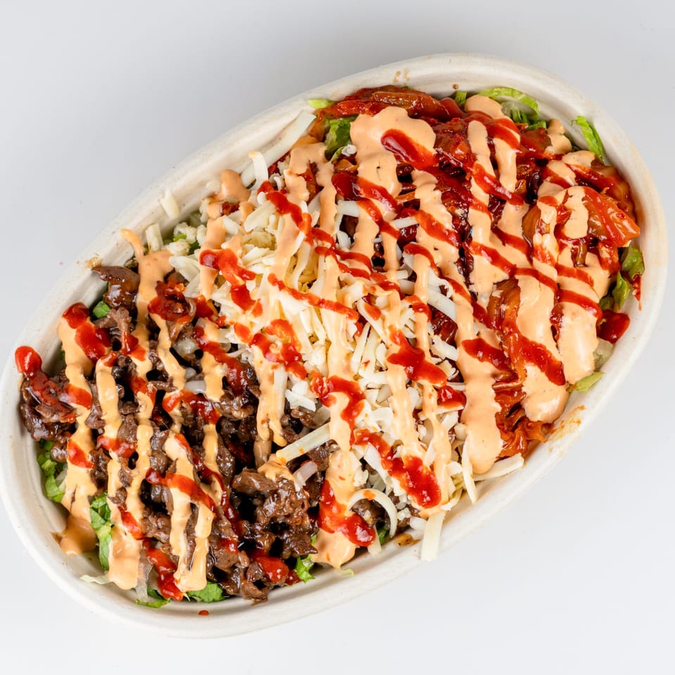 A Kudo Society Cafe bowl with beef, kimchi, shredded cheese, and two sauces.