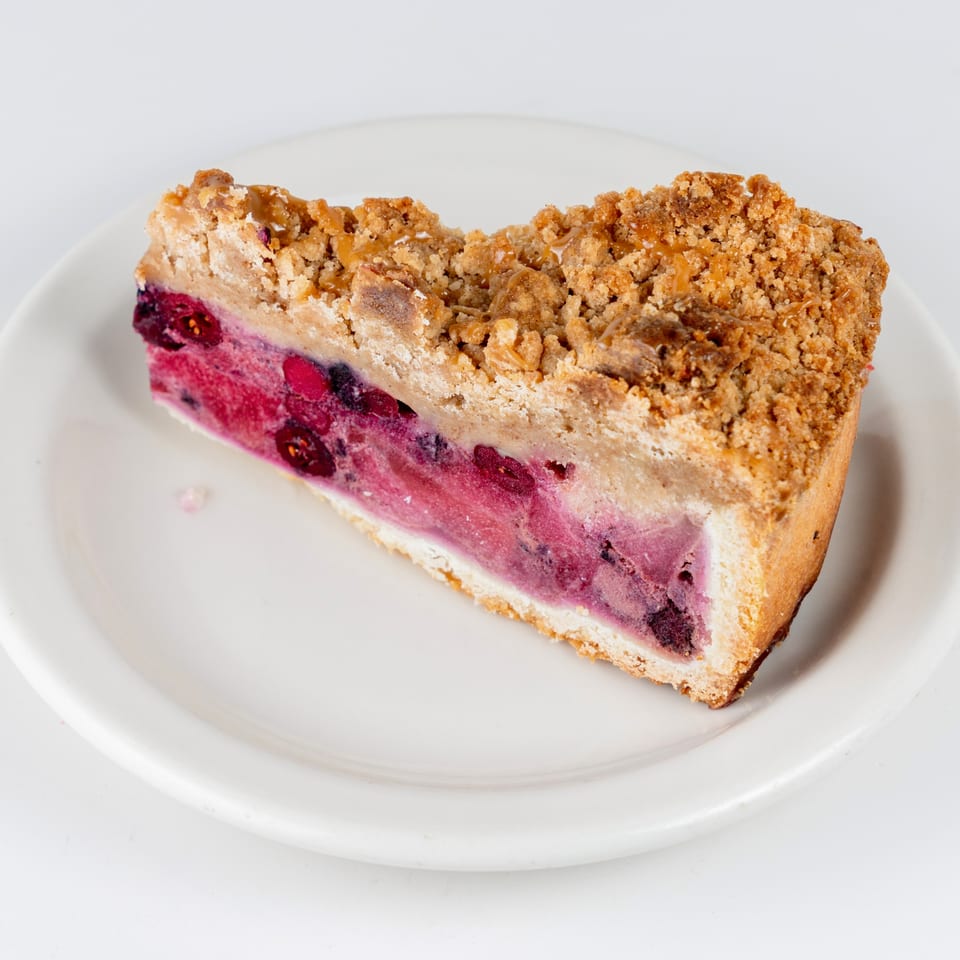 A slice of berry crumble cake with a thick, pink berry filling and a crumbly topping.