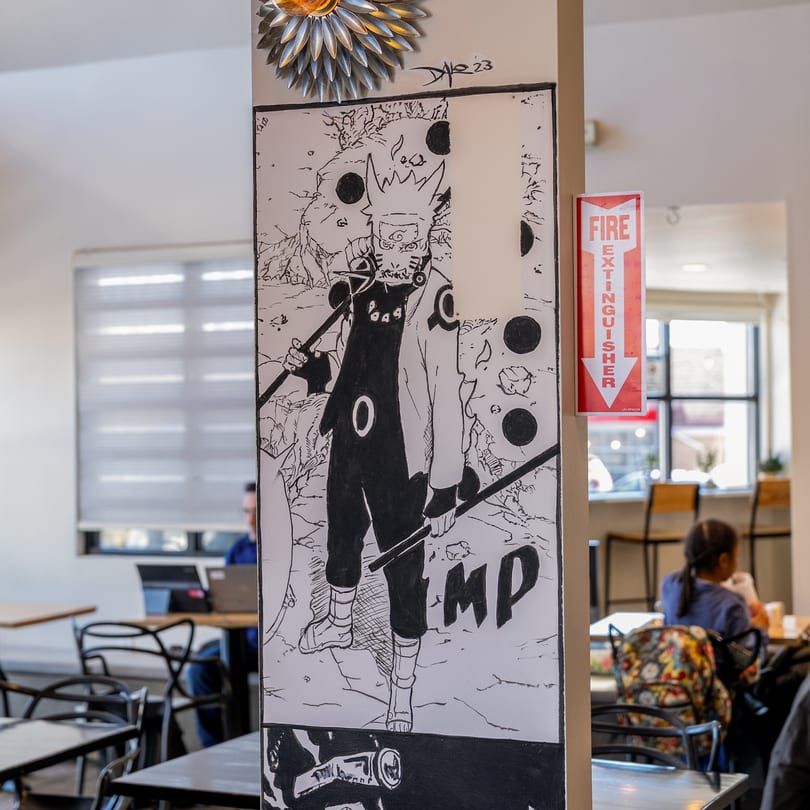 A Naruto anime drawing on a pillar in Kudo Society Cafe, with a fire extinguisher sign and blurred cafe interior.
