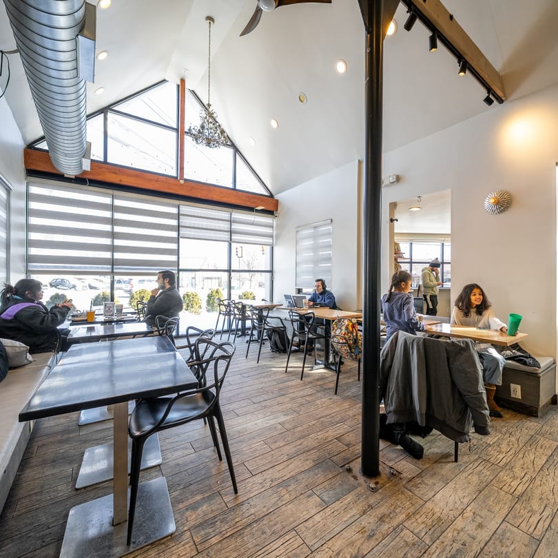 Customers relax and work in the bright, spacious Kudo Society Cafe with large windows.