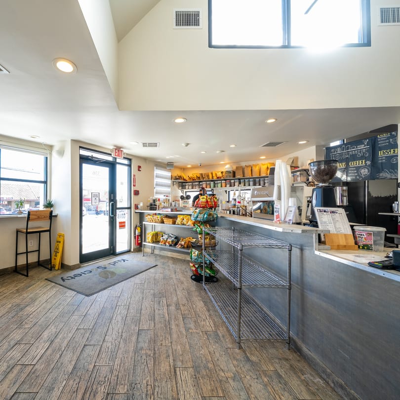 Interior of Kudo Society Cafe with a coffee bar, snack shelves, and wooden floors.