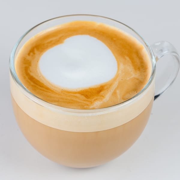 Close-up of a Kudo Society Cafe latte in a clear glass mug with a heart-shaped foam design.
