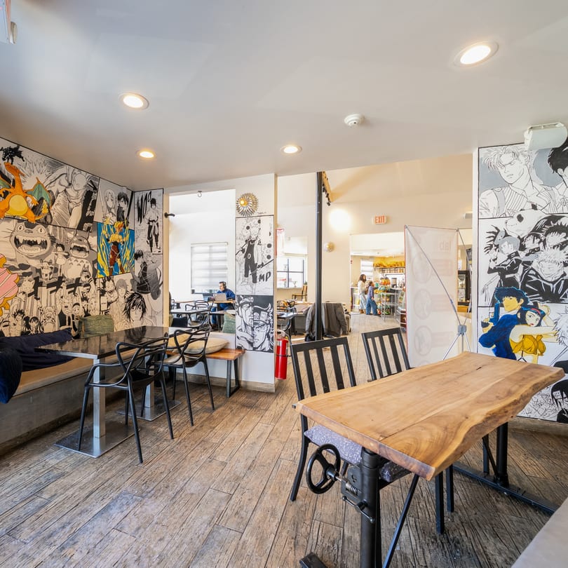 Kudo Society Cafe interior with anime-themed walls, wooden floors, and various seating arrangements.