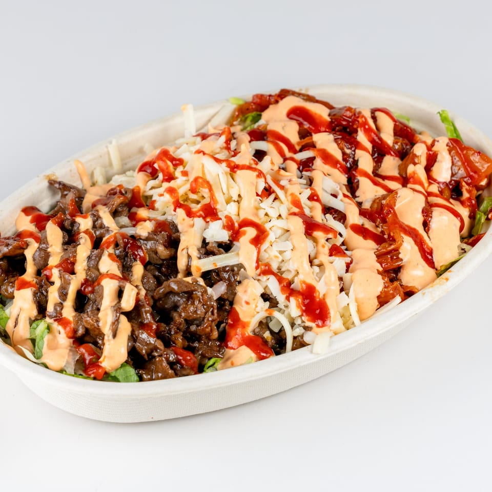 A close-up of a Kudo Society Cafe bowl filled with meat, cheese, and sauces.